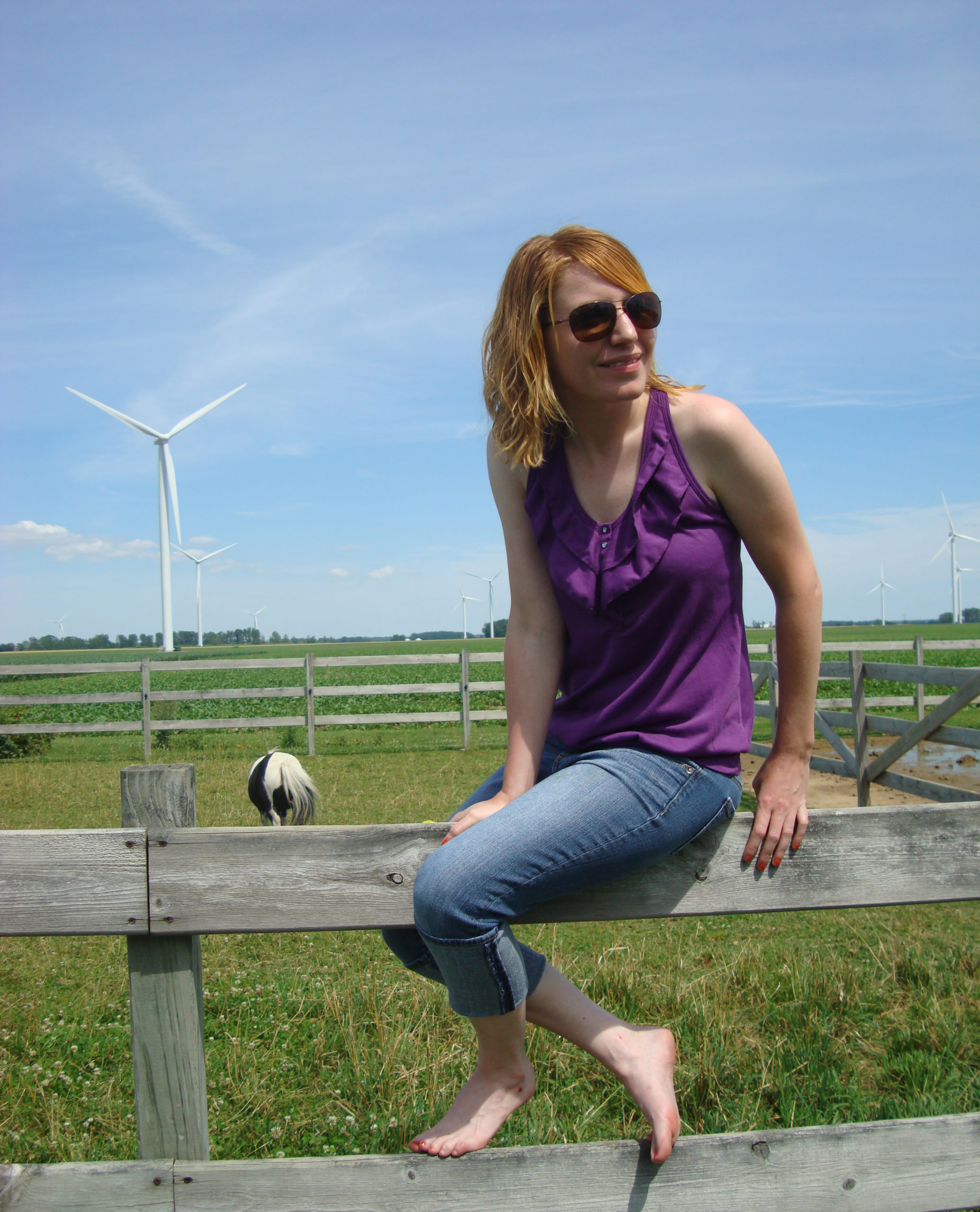 Katie Oeschger sitting on a horse fence with a horse in the background